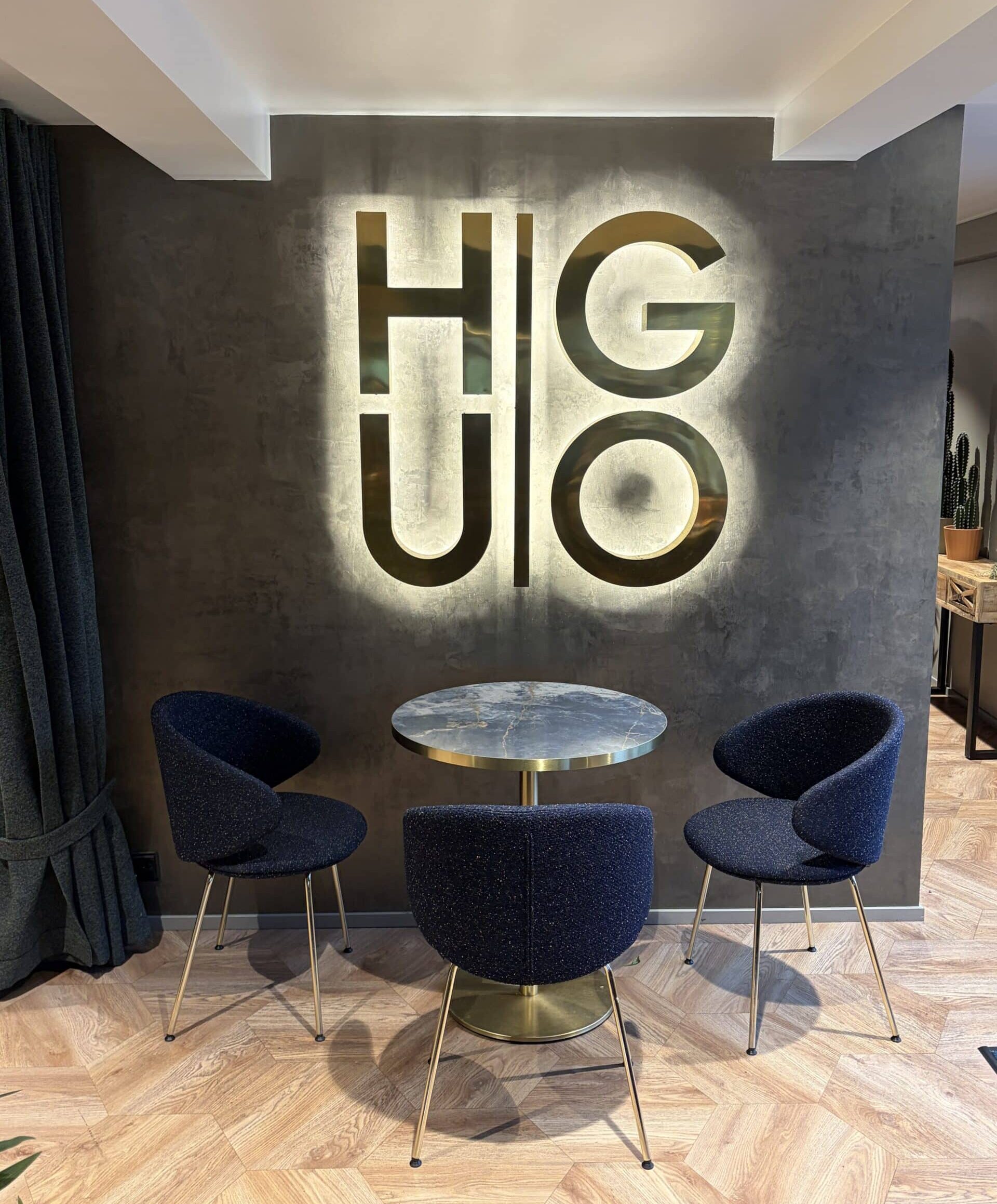 Takaa valaistu messinkinen HUGO-irtokirjainvalomainos hotellin aulassa